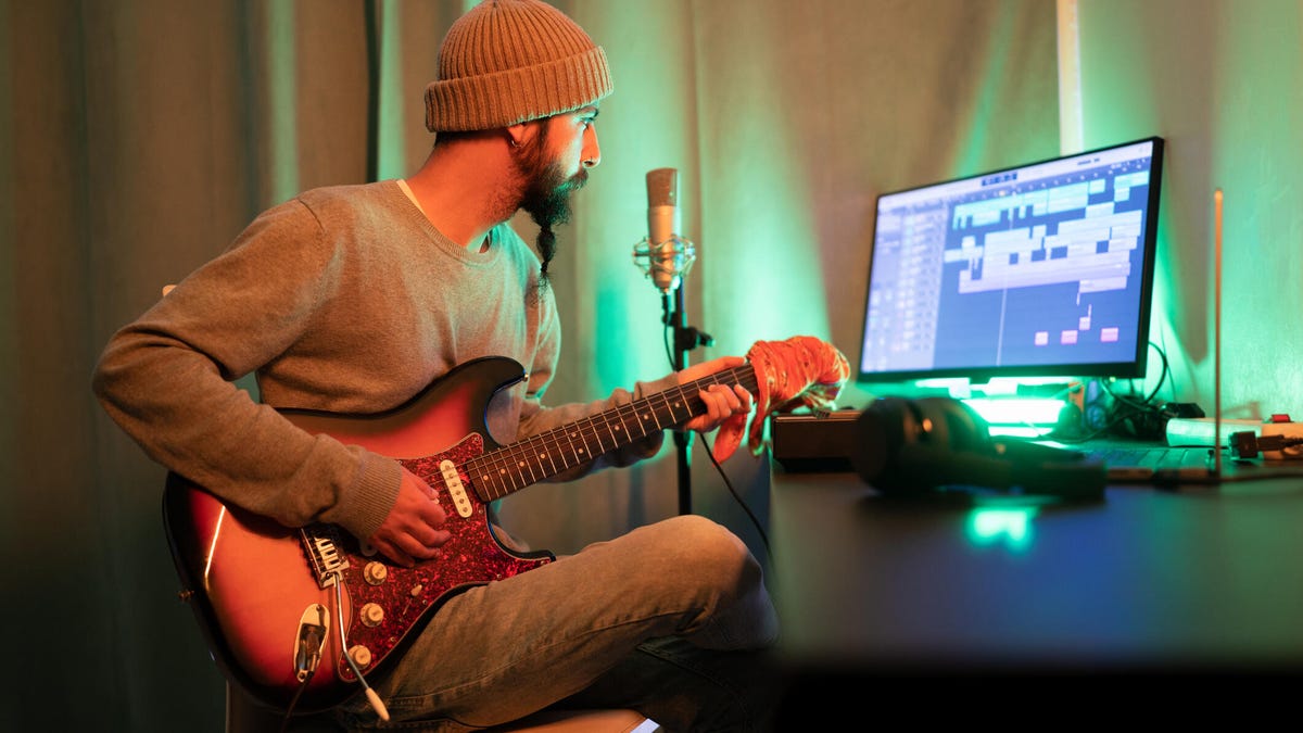 guy wearing beanie with guitar looking at a computer