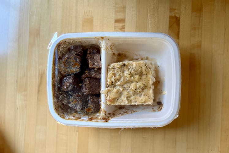 Short ribs and mac and cheese in a takeout container on a wooden table