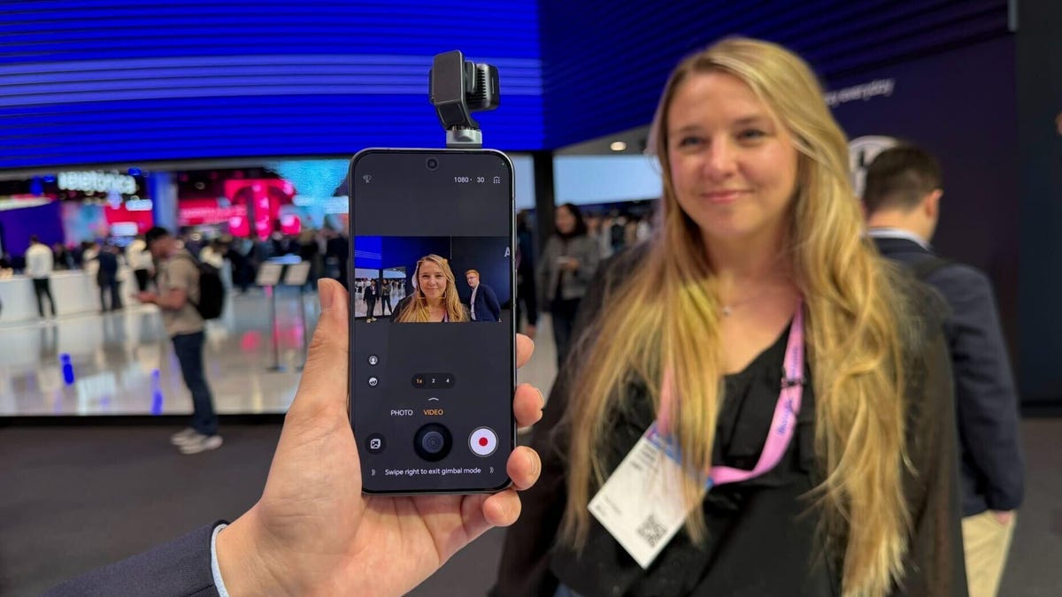 phone taking photo of tech journalist katie collins with blond hair and MWC badge at event