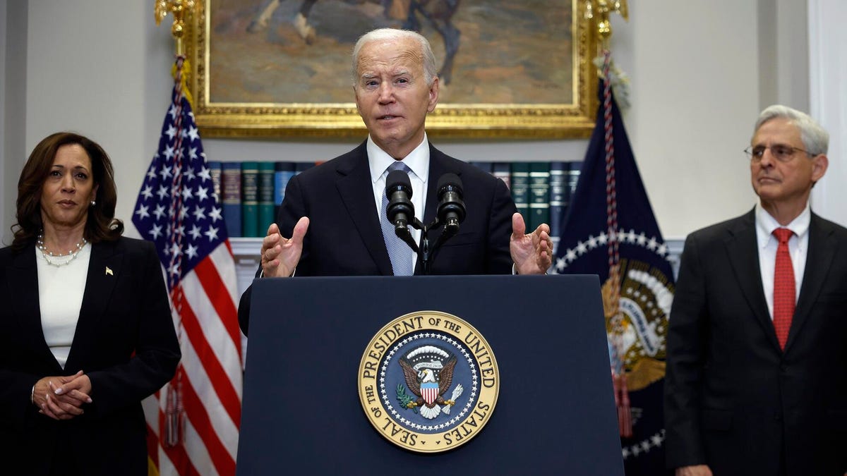 President Biden stands at a lectern emblazoned with the White House seal, flanked by Kamala Harris and Merrick Garland