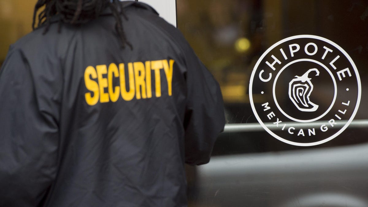 Man wearing a "security" jacket in front of a Chipotle outlet.