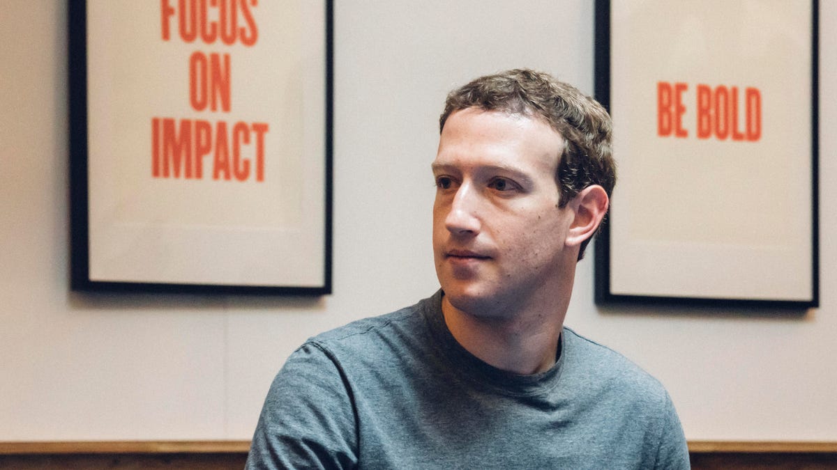 Facebook CEO Mark Zuckerberg in front of signs that say "focus on impact" and "be bold."