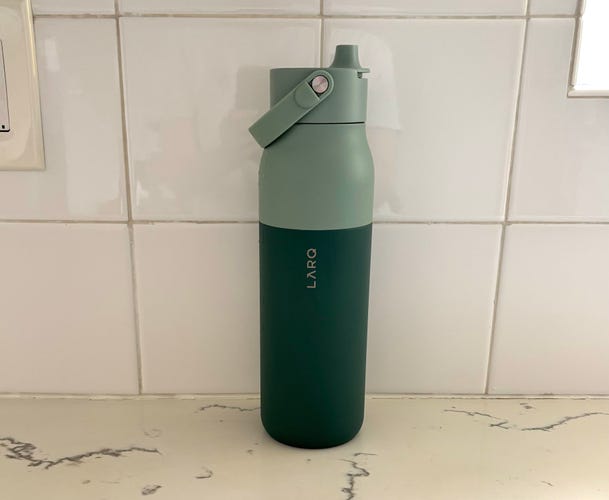 The green LARQ Self Cleaning Water Bottle on a white marble countertop with a white tile background.
