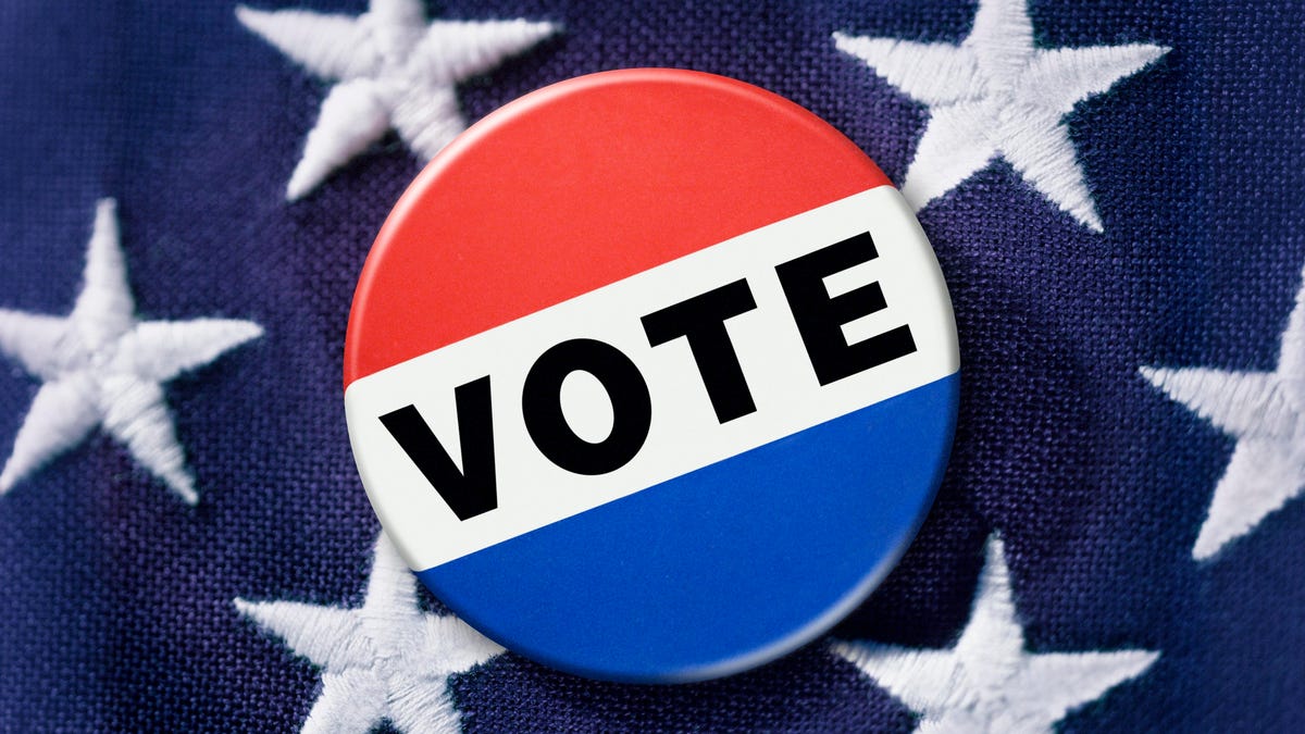 A red, white, and blue "Vote" pin against a background of American flag stars