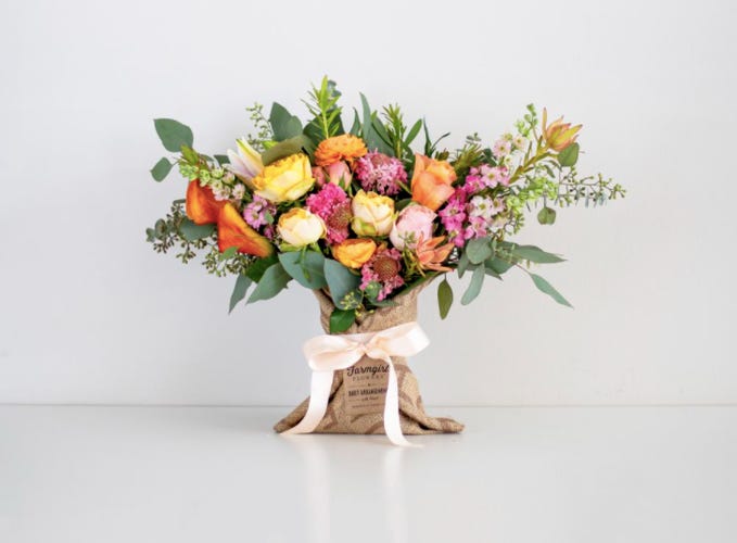 a bouquet of different colored flowers in a burlap sack with a ribbon