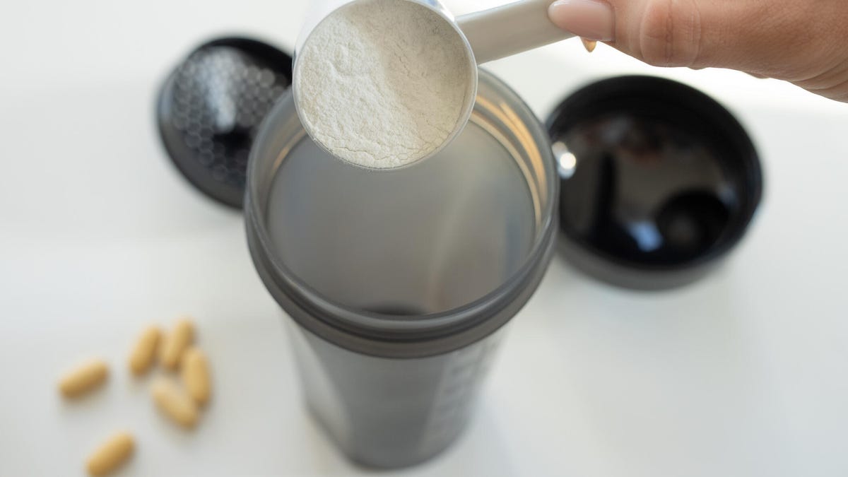 A hand pouring a scoop of creatine powder into a blender container.