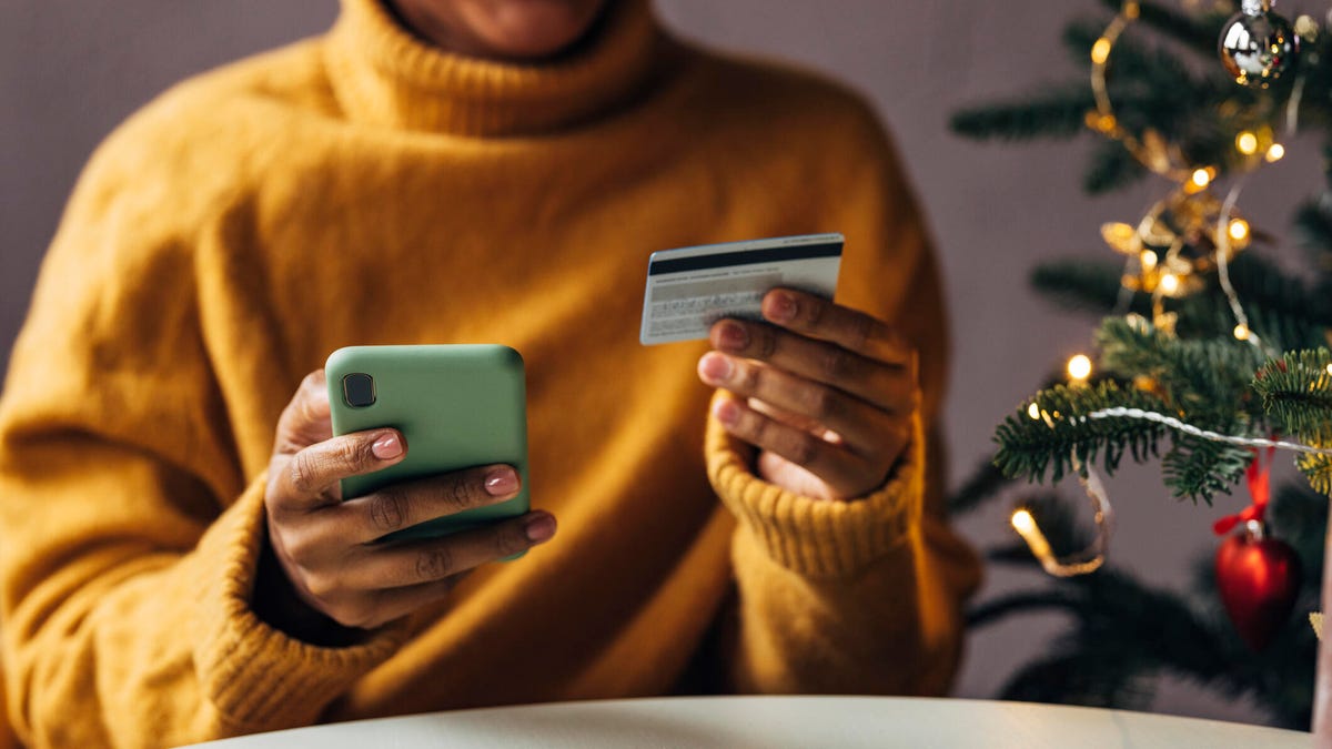 A person smiles at her credit card next to a Christmas tree.