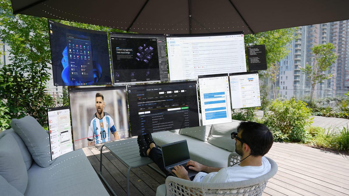 A man leaning back and working with virtual displays wearing AR glasses and a laptop