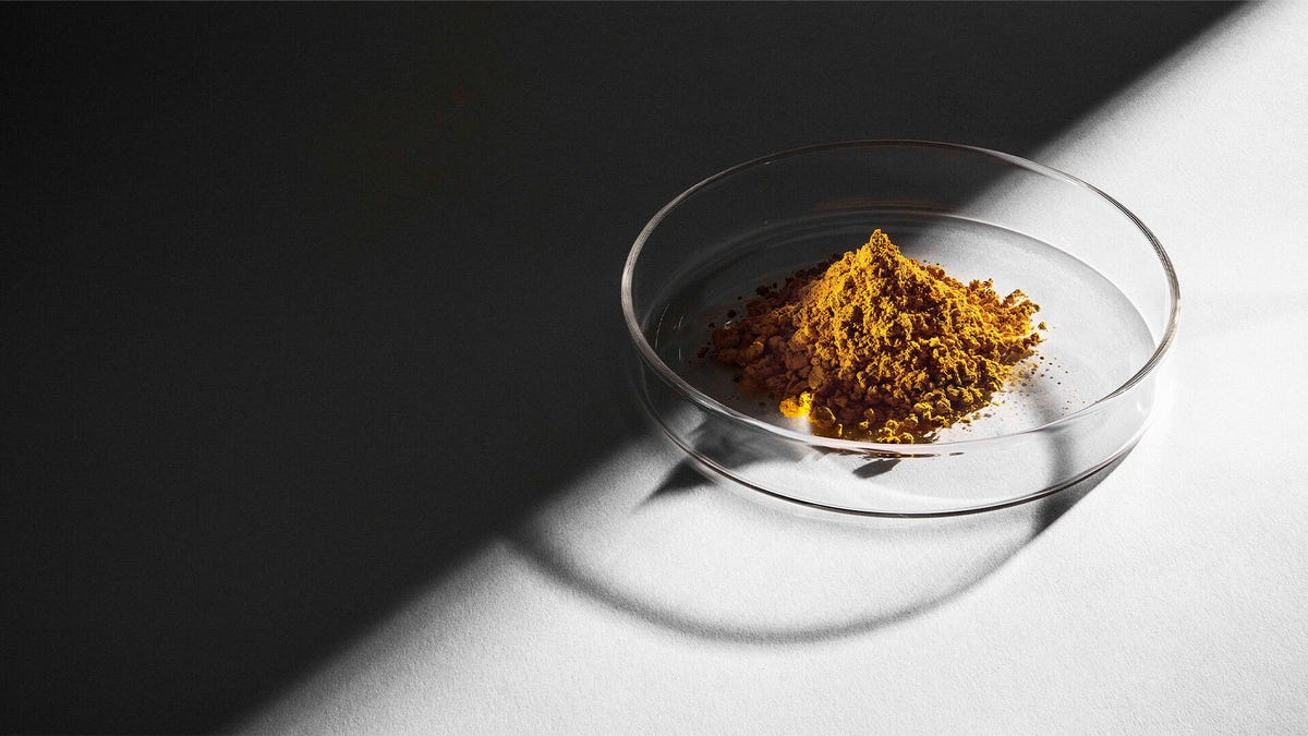 A petri dish with a pile of gold-colored powder on a white desk