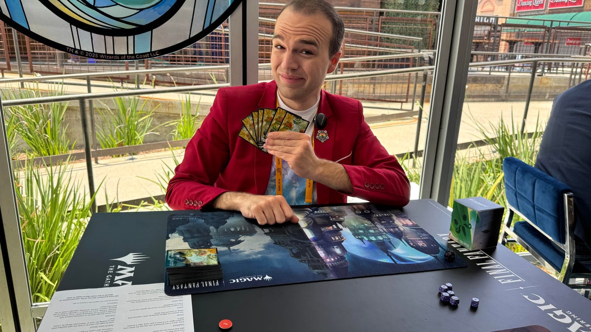 A man in a red suit holds a set of Magic cards at a table with a Final Fantasy-themed playing mat and cards.