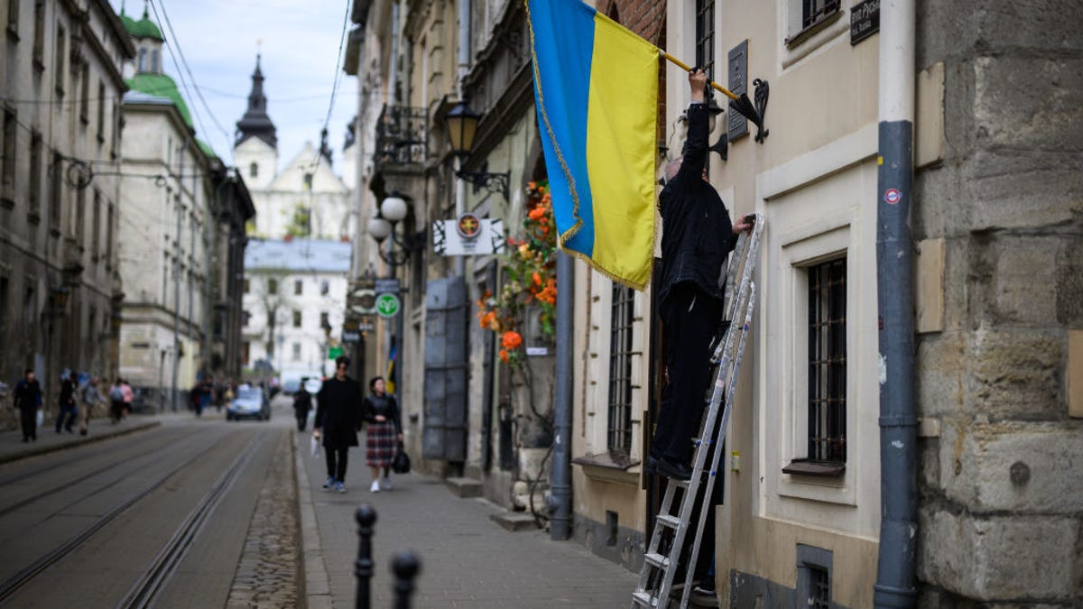 A man climbs a ladder to hang a Ukrainian flag outside a business in Lviv, Ukraine.