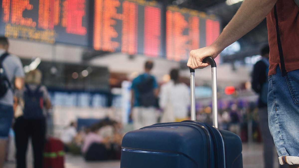 Traveler with suitcase standing in front of an airport flight board