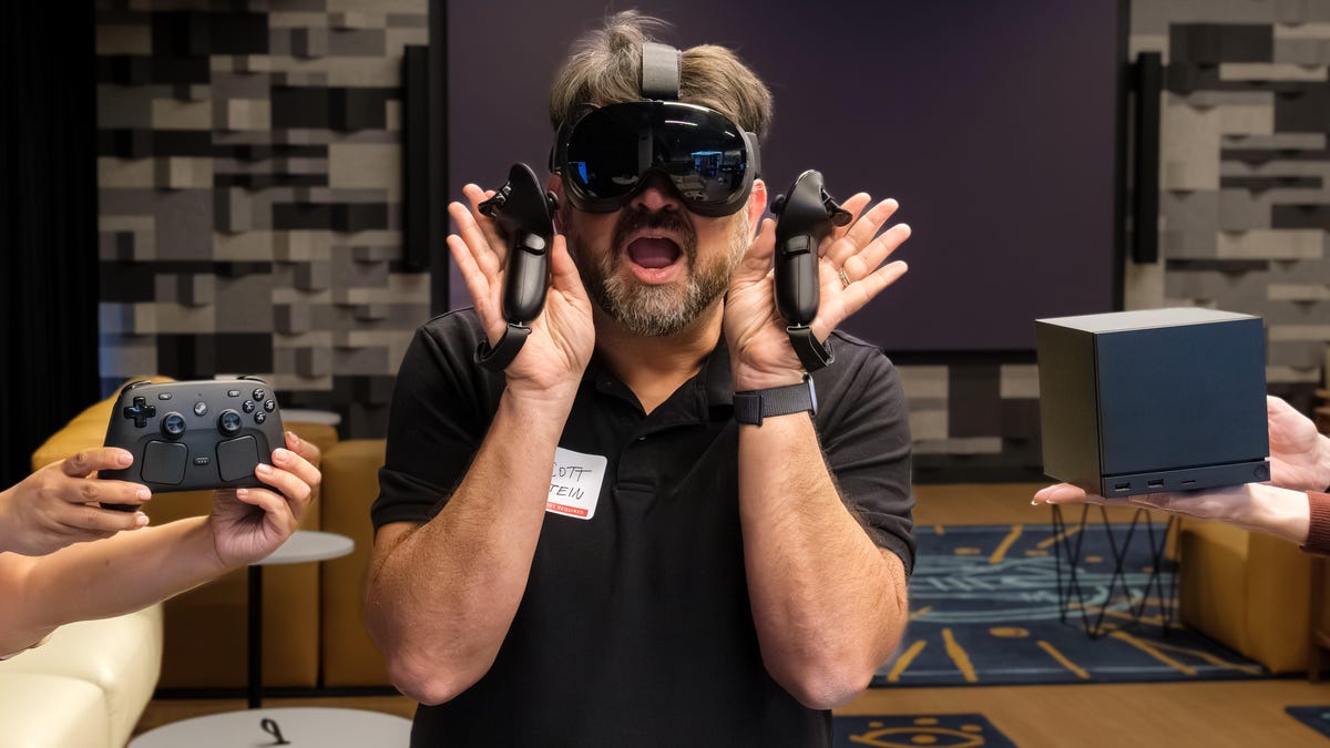 CNET's Scott Stein with Valve Steam Frame VR headset on face, and Steam Controller and Steam Machine to his left and right