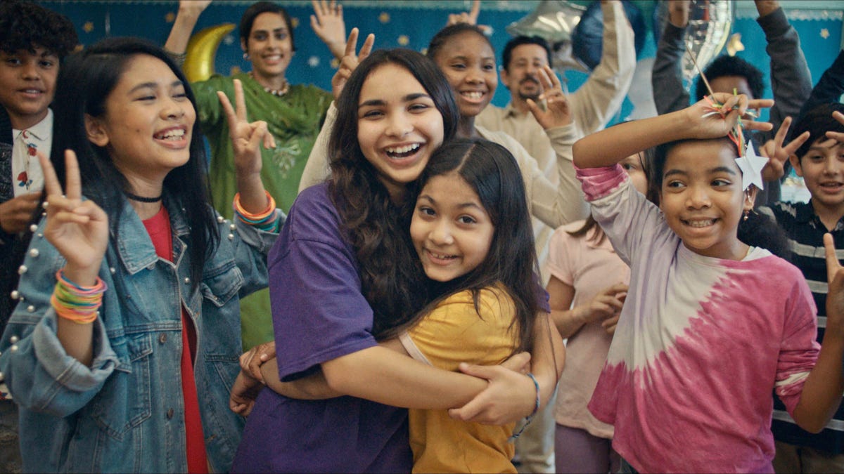 Sisters Ameena and Zainab smile and hug each other while surrounded by celebrating classmates.
