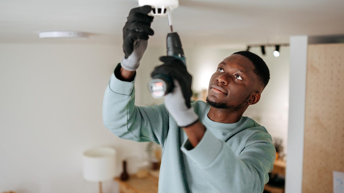 A man screws in a sensor into a home ceiling.