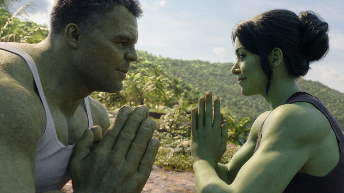 She-Hulk, a woman with green skin and superpowers, adopts a yoga pose and smiles at the bigger but equally green Incredible Hulk.