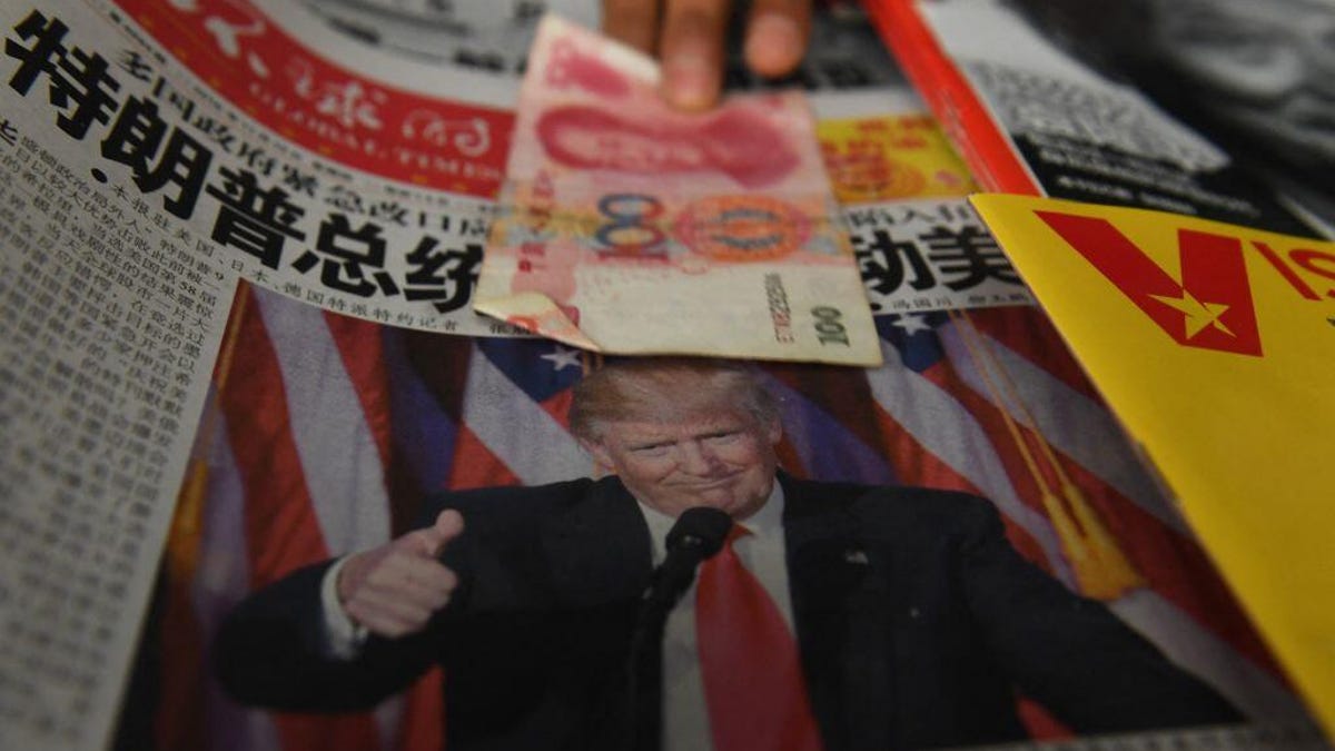 A vendor picks up a 100 yuan note above a newspaper featuring a photo of Donald Trump, at a newsstand in Beijing