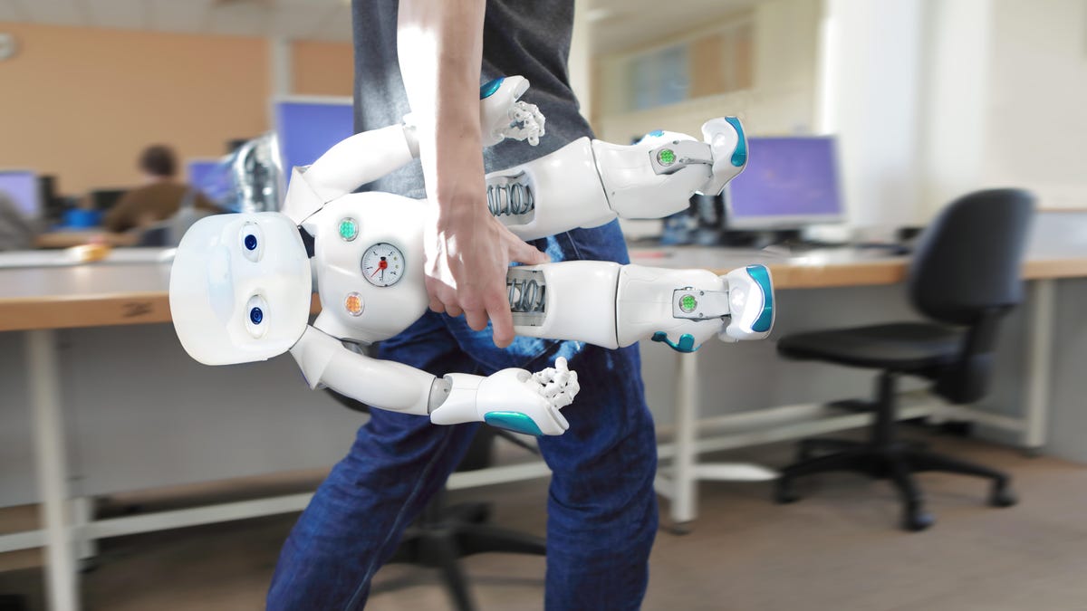 A man carries a robot through an office.