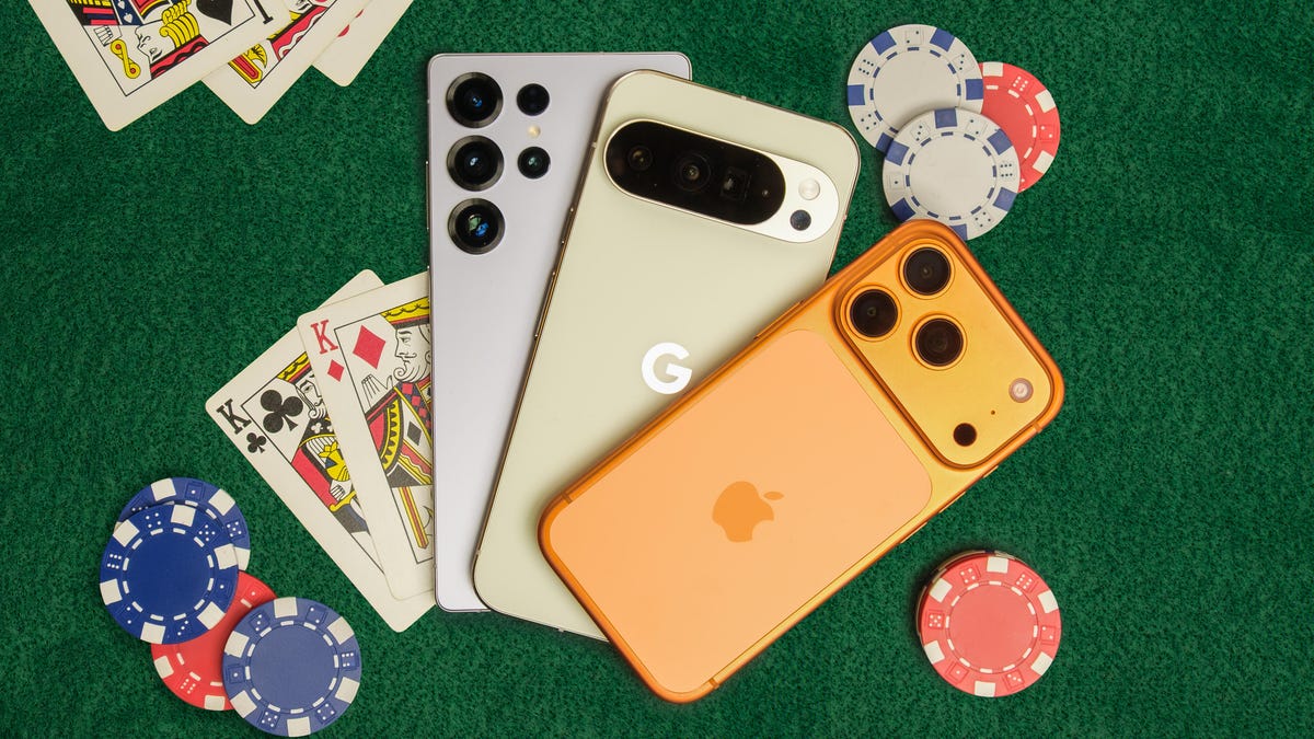 Three phones on a card table with cards and poker chips around them.