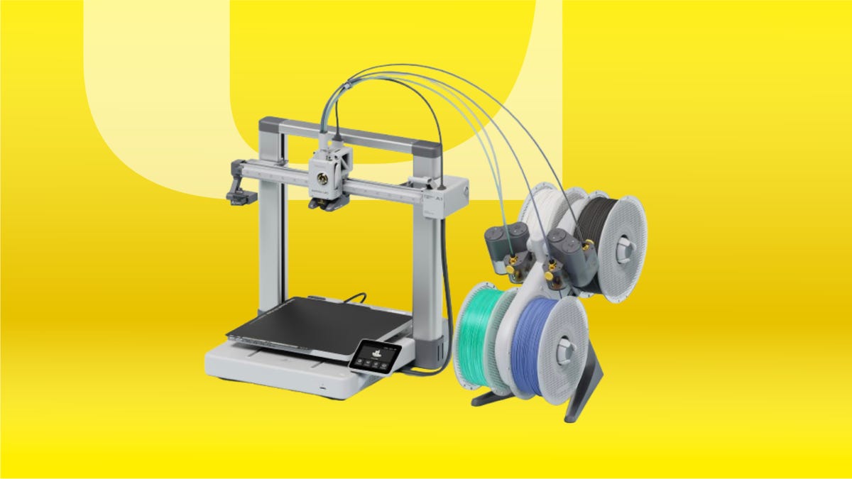 Silver 3D printer with black working table. To the right: wheels with black, white, mint green and blue filaments. Background: yellow gradient.