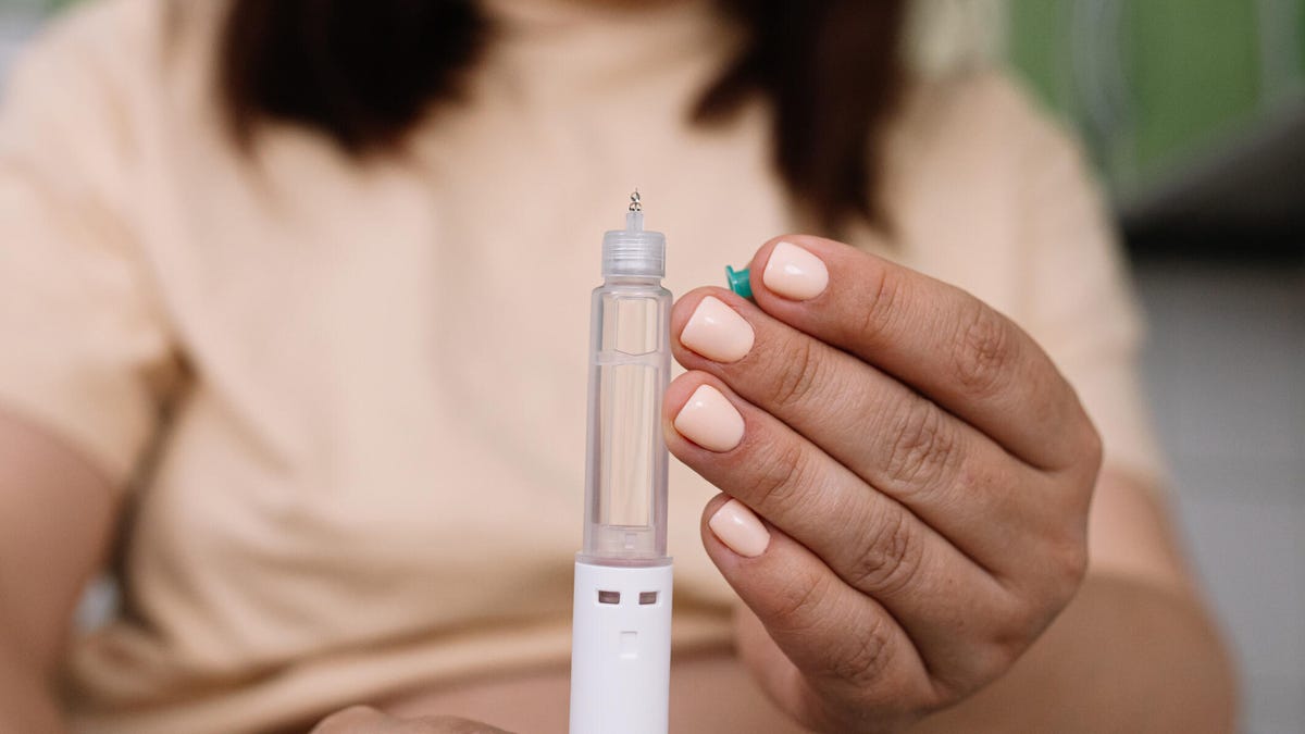 A person in a light peach tee holding a semaglutide injection pen with a light peach-colored manicure.