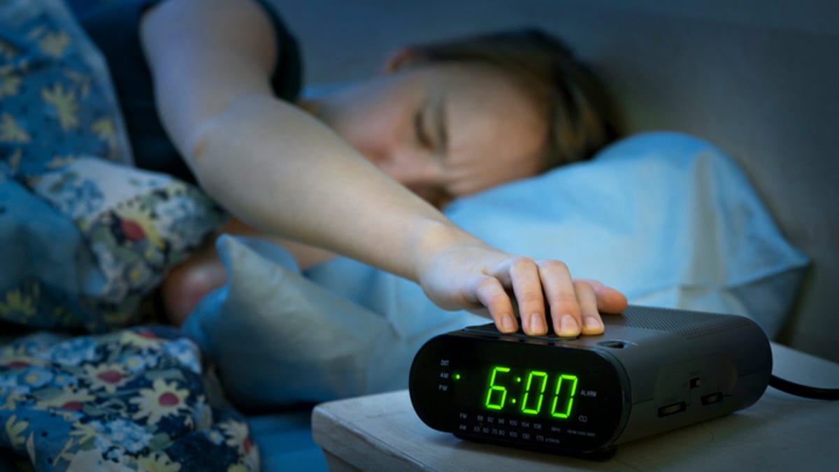 Young woman reaching to her bedside table and snoozing her alarm clock