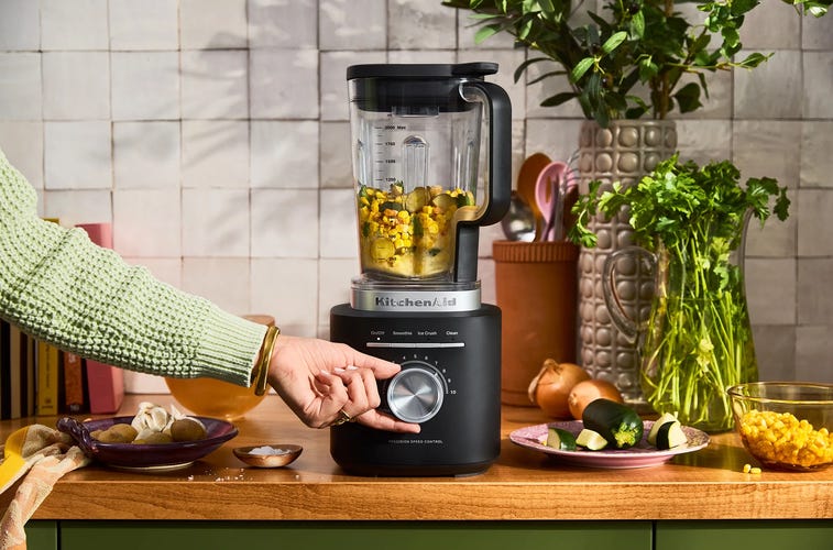 a woman turning on a black blender on a wooden countertop in a kitchen