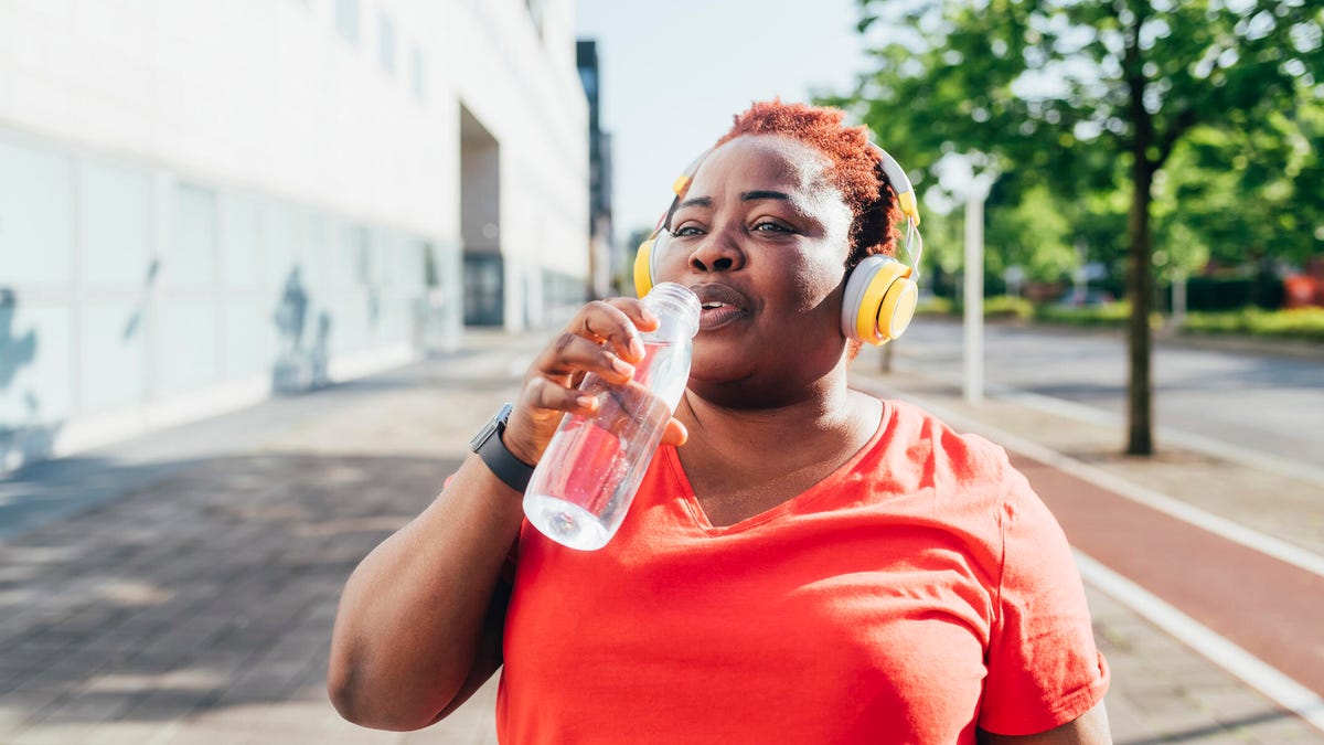 person with headphones on a run on the sidewalk drinking out of a water bottle