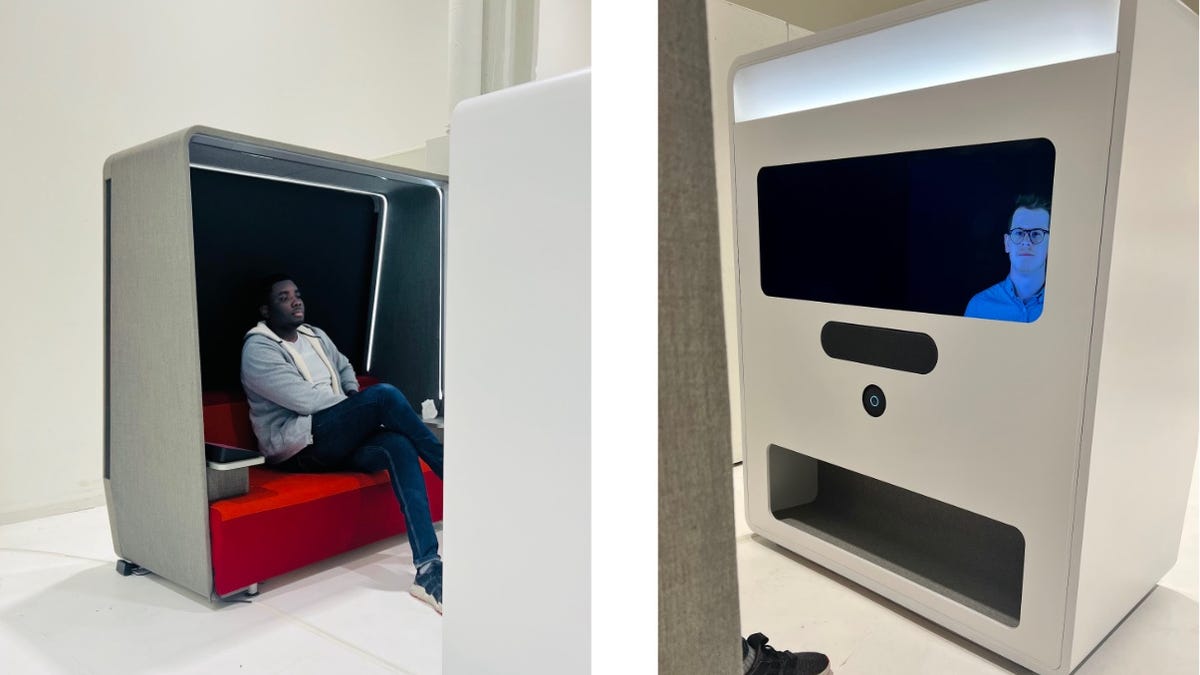 A man on a small red sofa talking with a TV screen with a floating face inside