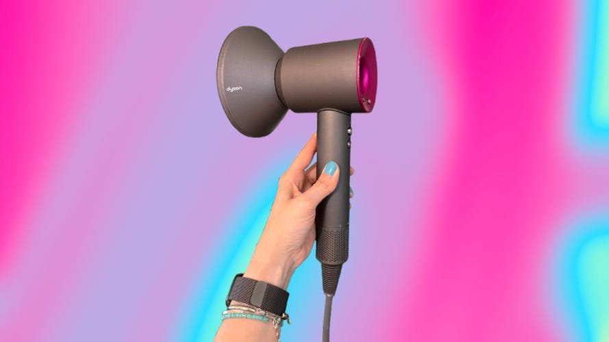 A hand holding the Dyson Supersonic dryer over a purple, magenta and neon blue abstract background.