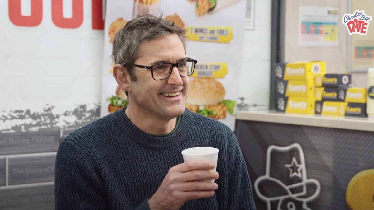 Louis Theroux drinking from a white styrofoam cup while smiling.