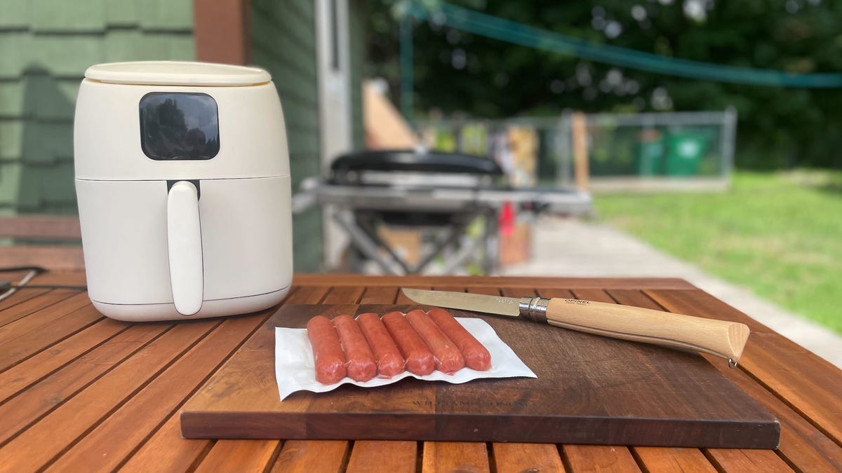 air fryer and hot dogs sit on a cutting board out on a patio table in summer