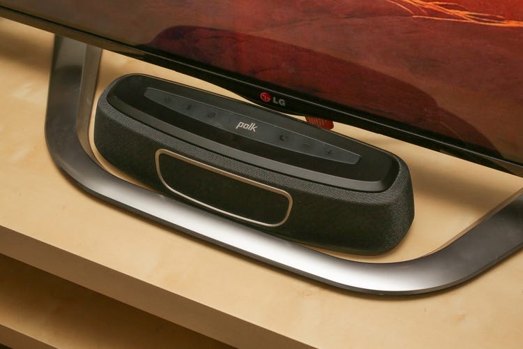 The Polk Magnifi Mini soundbar under an LG television on top of a wooden console stand. 