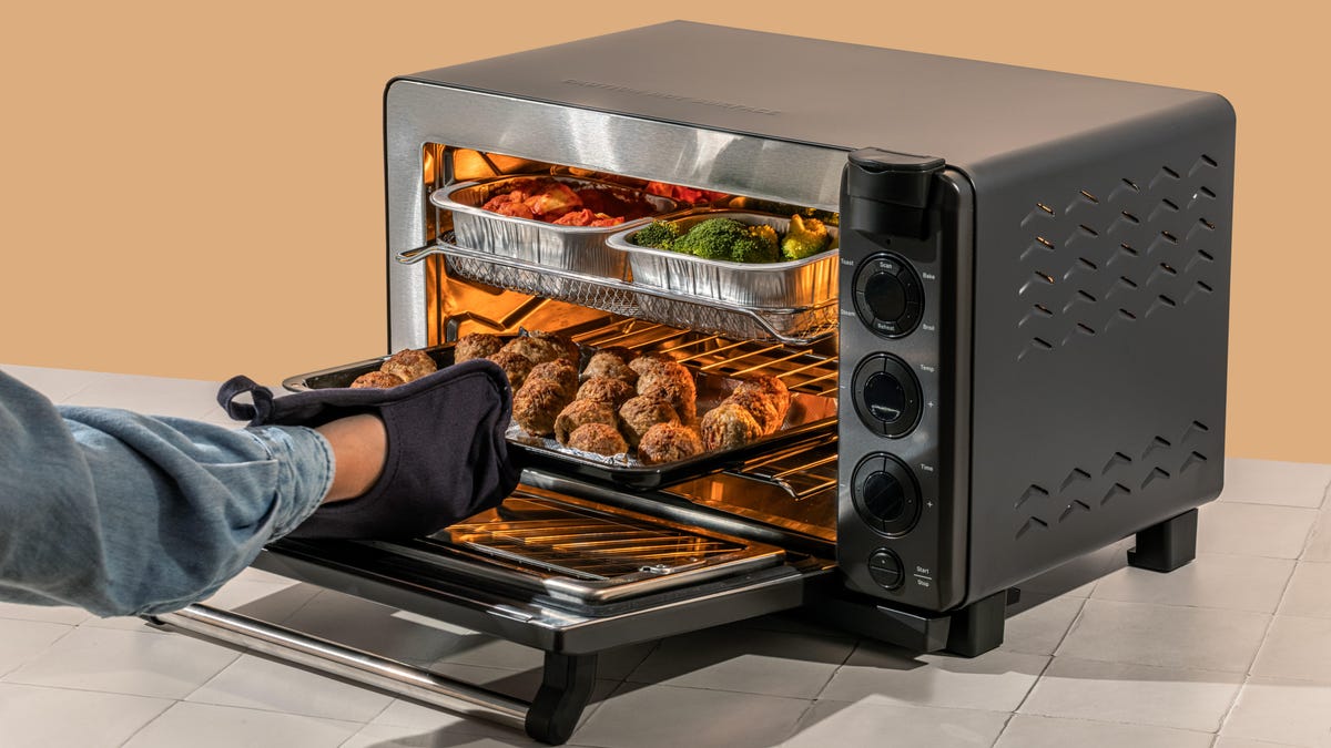 A person putting meatballs into a black toaster oven