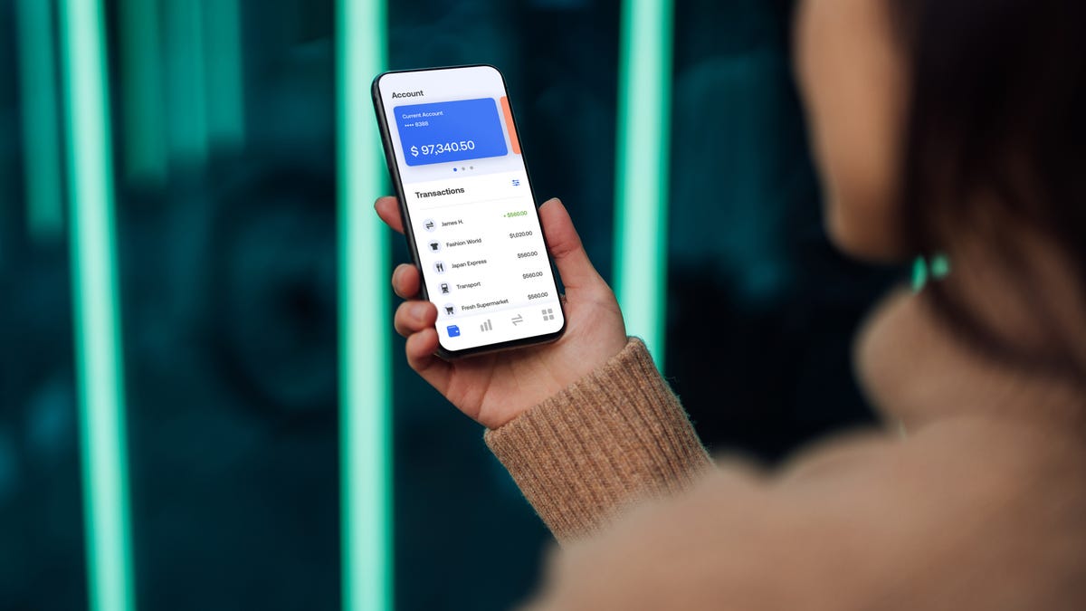 Over the shoulder view of a young woman using mobile phone against futuristic holographic background. New ways of managing personal finance.