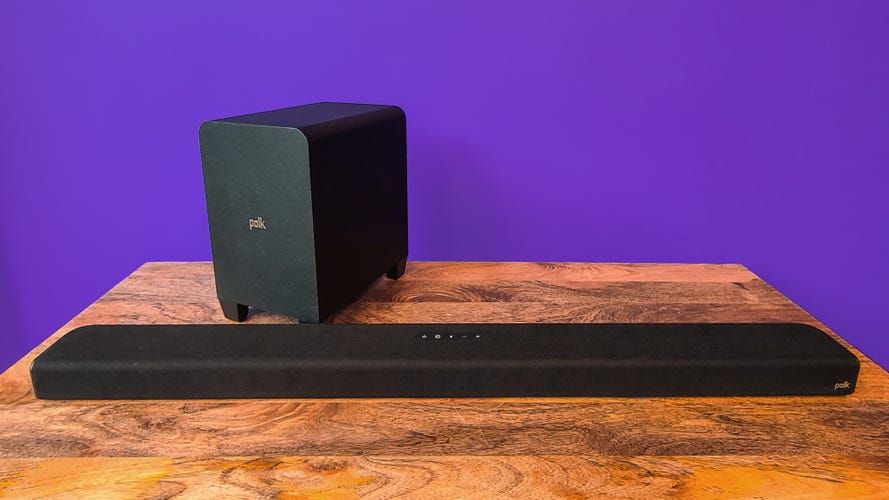 Polk Signa S4 Soundbar and Subwoofer on a wooden table in front of a purple background. 