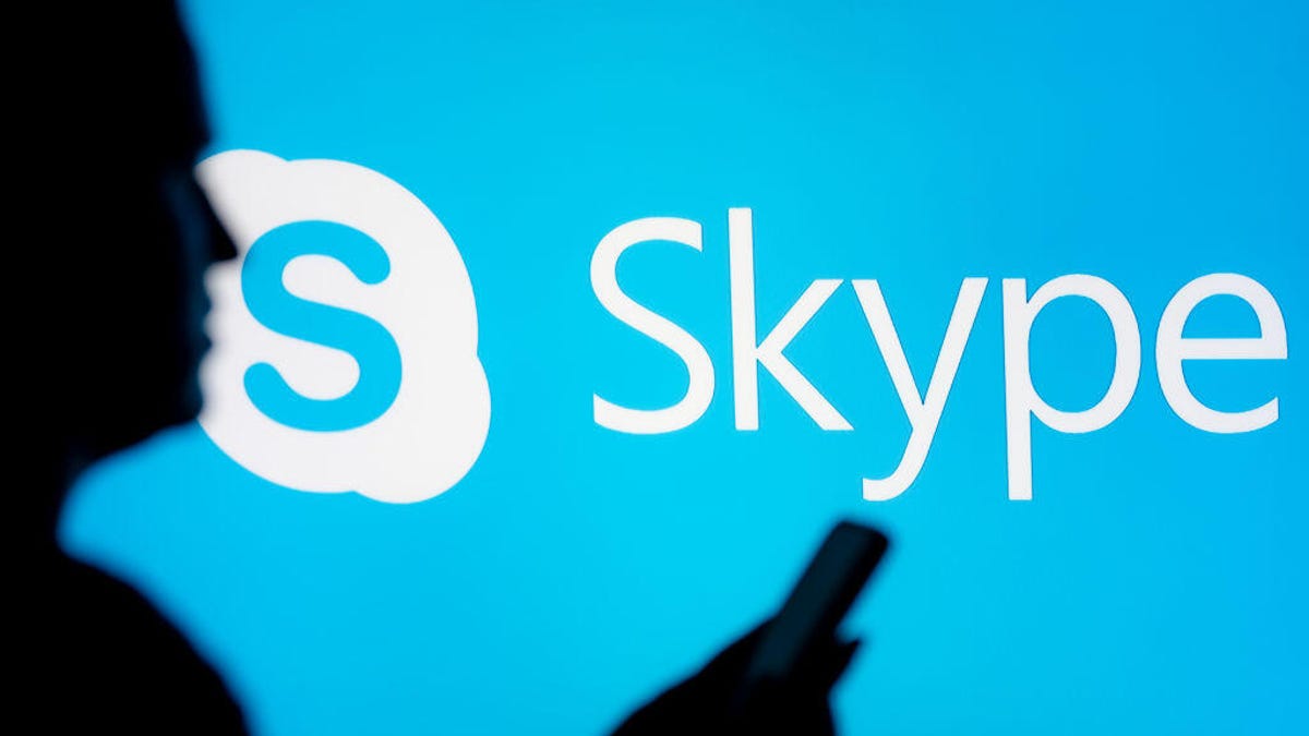 In this photo illustration, a woman seen looking at a smartphone with a Skype logo displayed in the background.