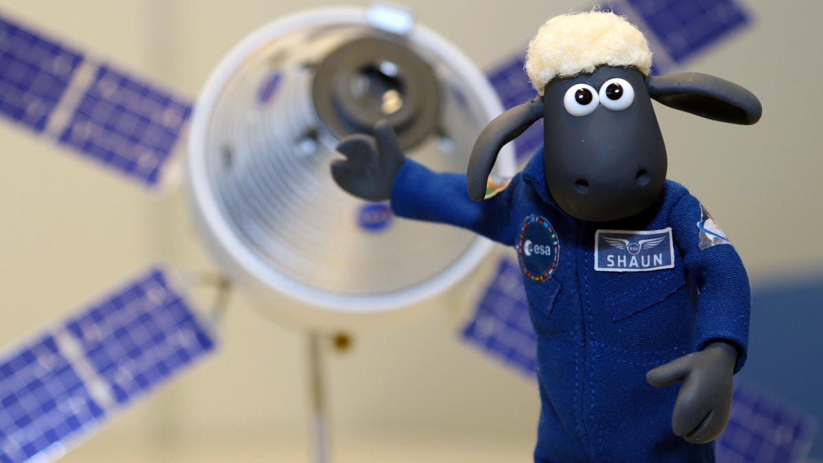 Shaun the Sheep in a flight suit, gesturing toward a model of a satellite