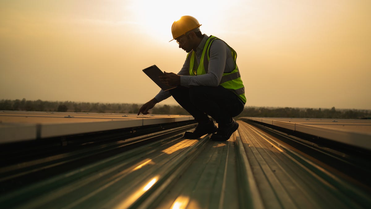 worker in a hard hat examining power lines, the sun behind him