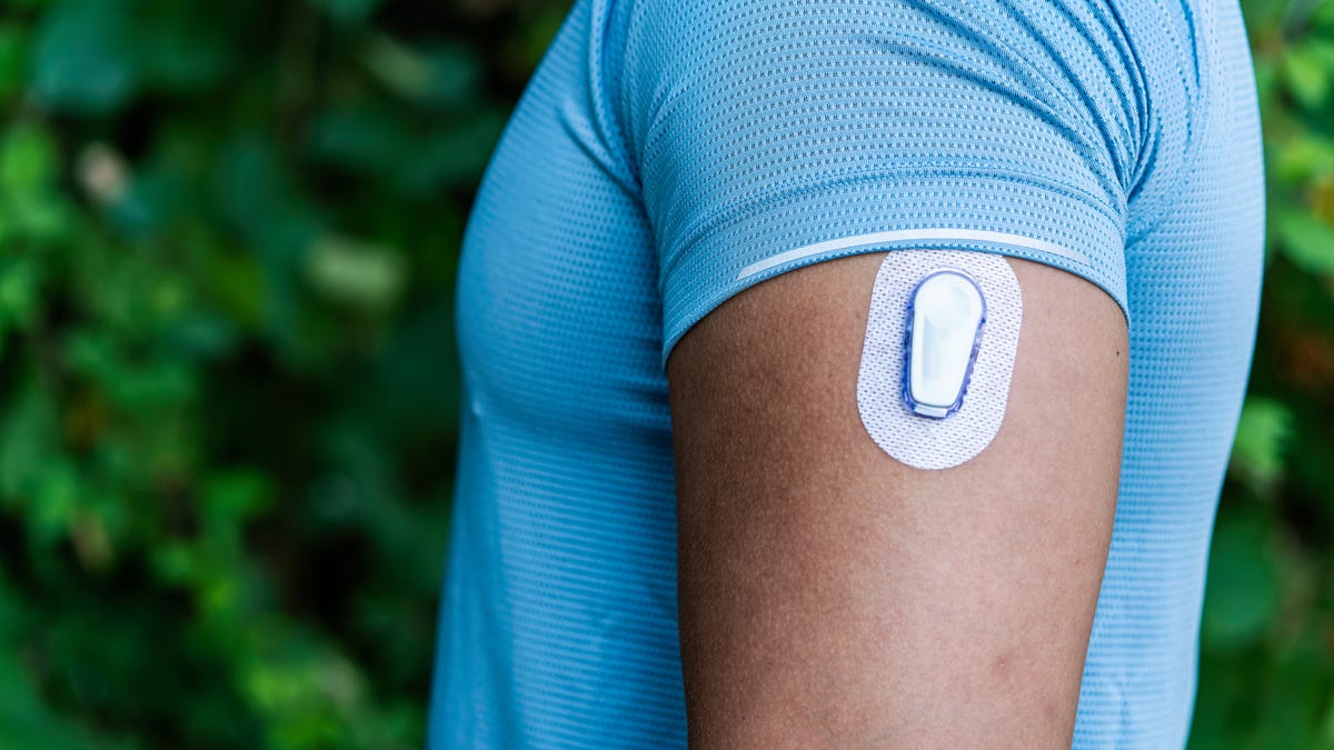 A man in a light blue shirt wears a continuous glucose monitor