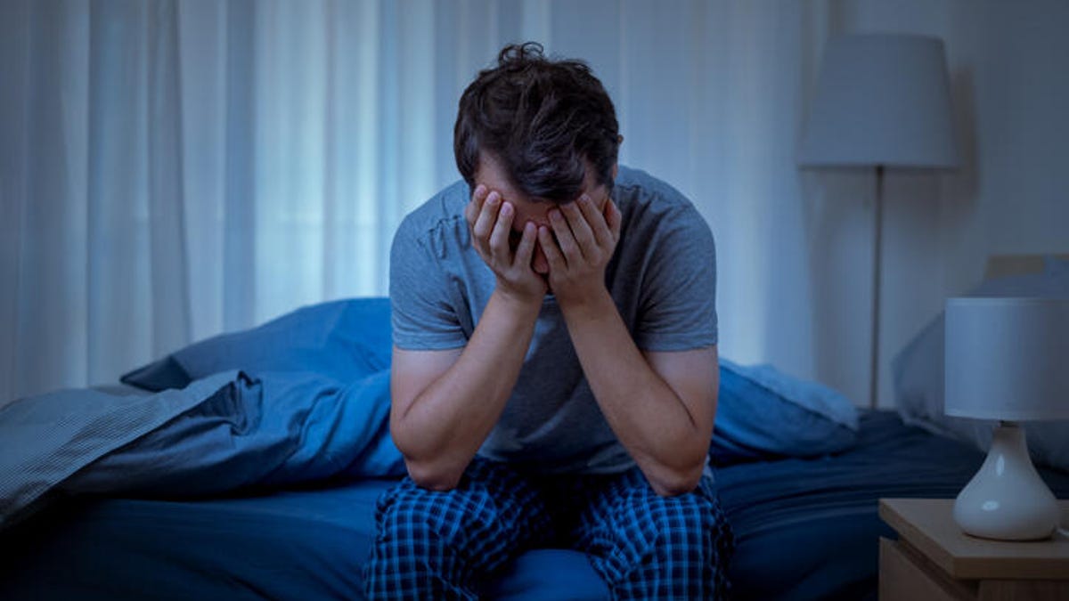 Man sitting on the edge of his bed with his head in his hands.
