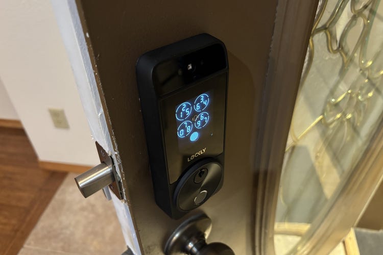 A Lockly Visage lock with keypad glowing on an open brown door.