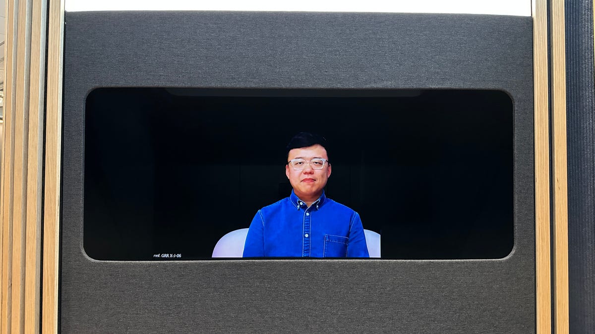 A man looking through a window sized hole in a wall, having a video chat