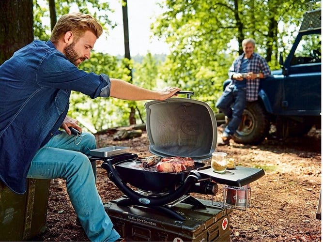 A man cooks meat on a grill in the woods