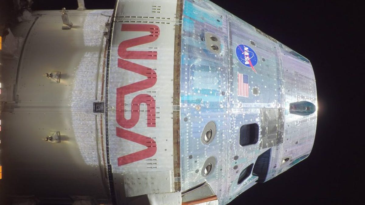 Conical silver and white Orion spacecraft selfie with dark space beyond and NASA in big red letters.