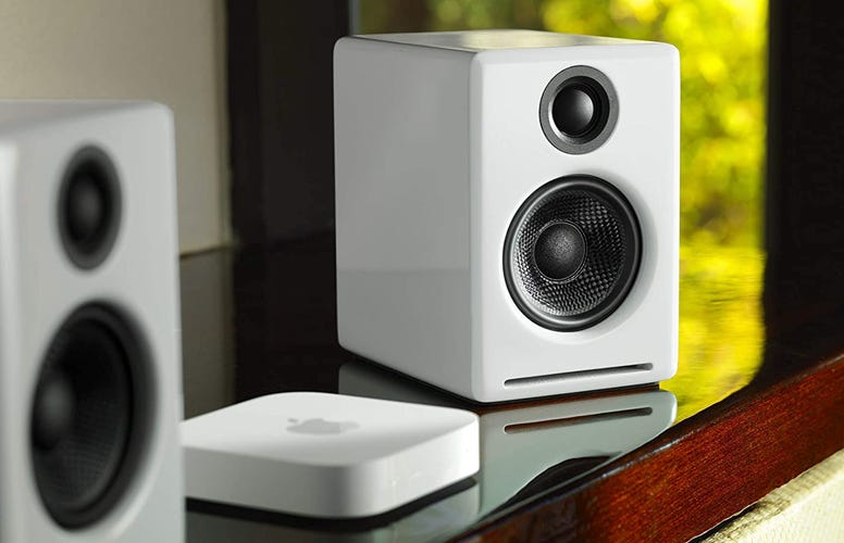 The white AudioEngine A2 speakers on top of a reflective wooden surface, complete with Apple TV. 