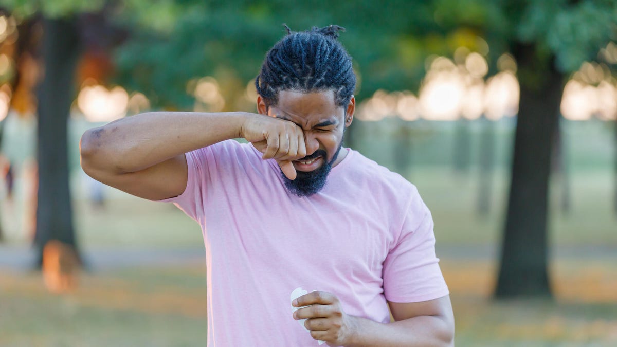 Man rubbing his eye in a park