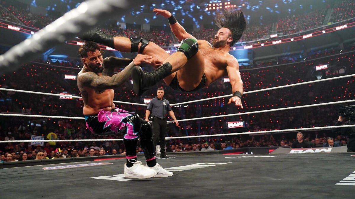 One man kicks another in a professional wrestling ring.