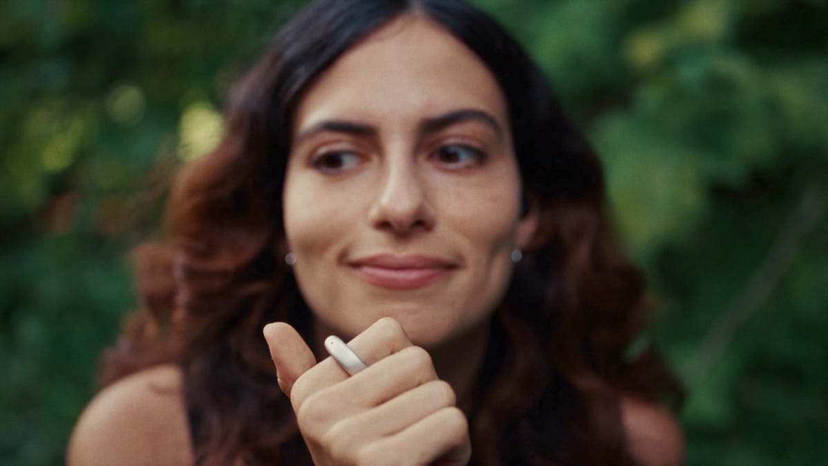 A woman with her right hand raised to her chin, with a silver ring on her index finger.