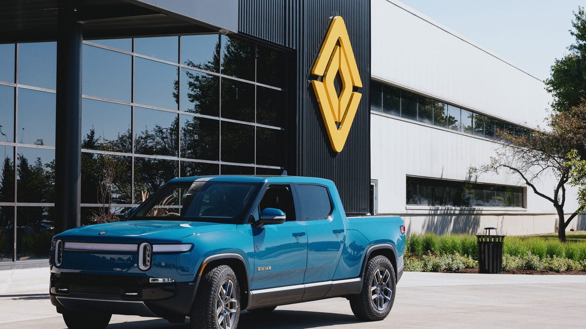 A blue Rivian R1T pickup truck parked in front of an office building
